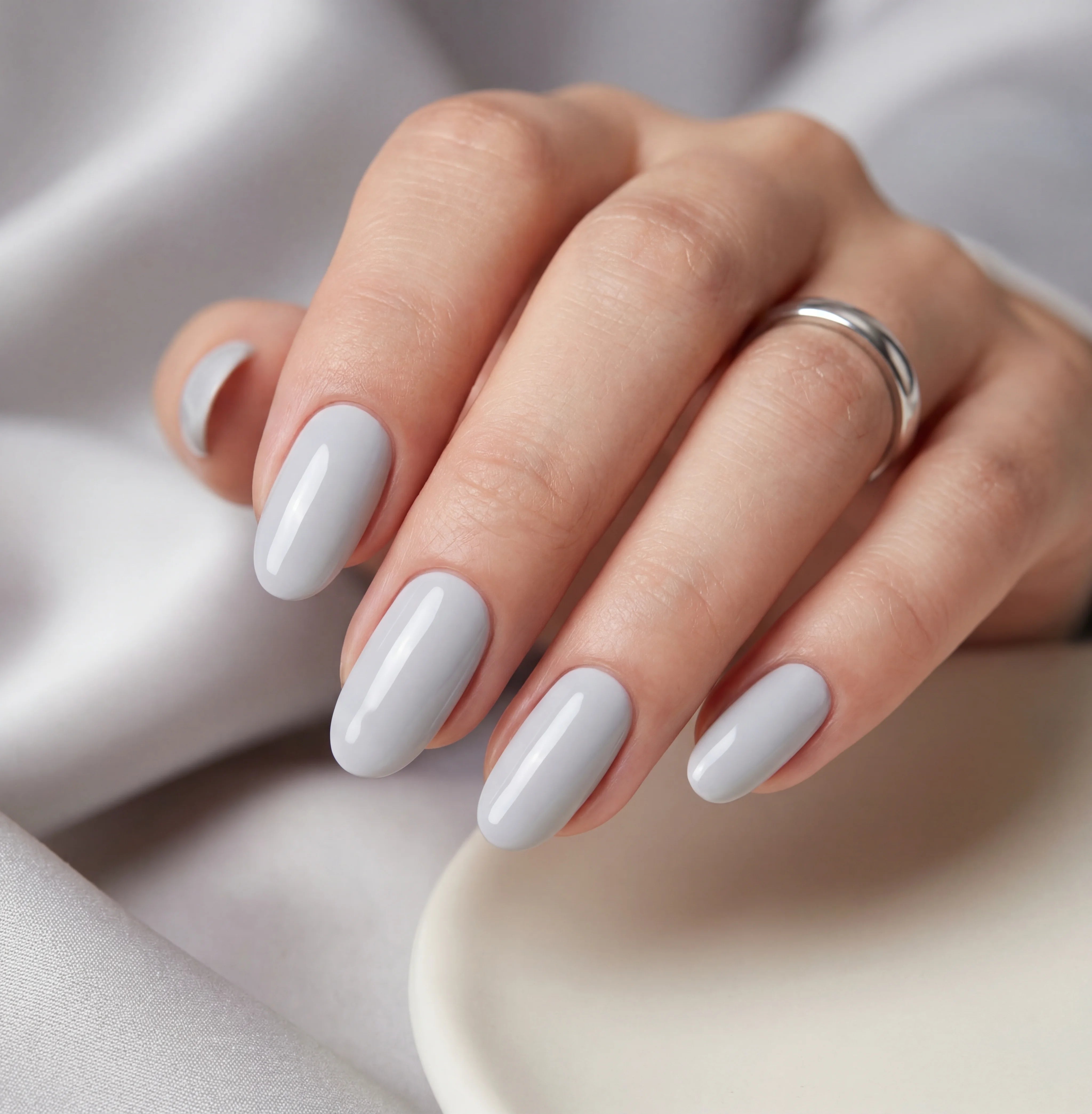 Hand with light gray nail polish on a soft fabric background